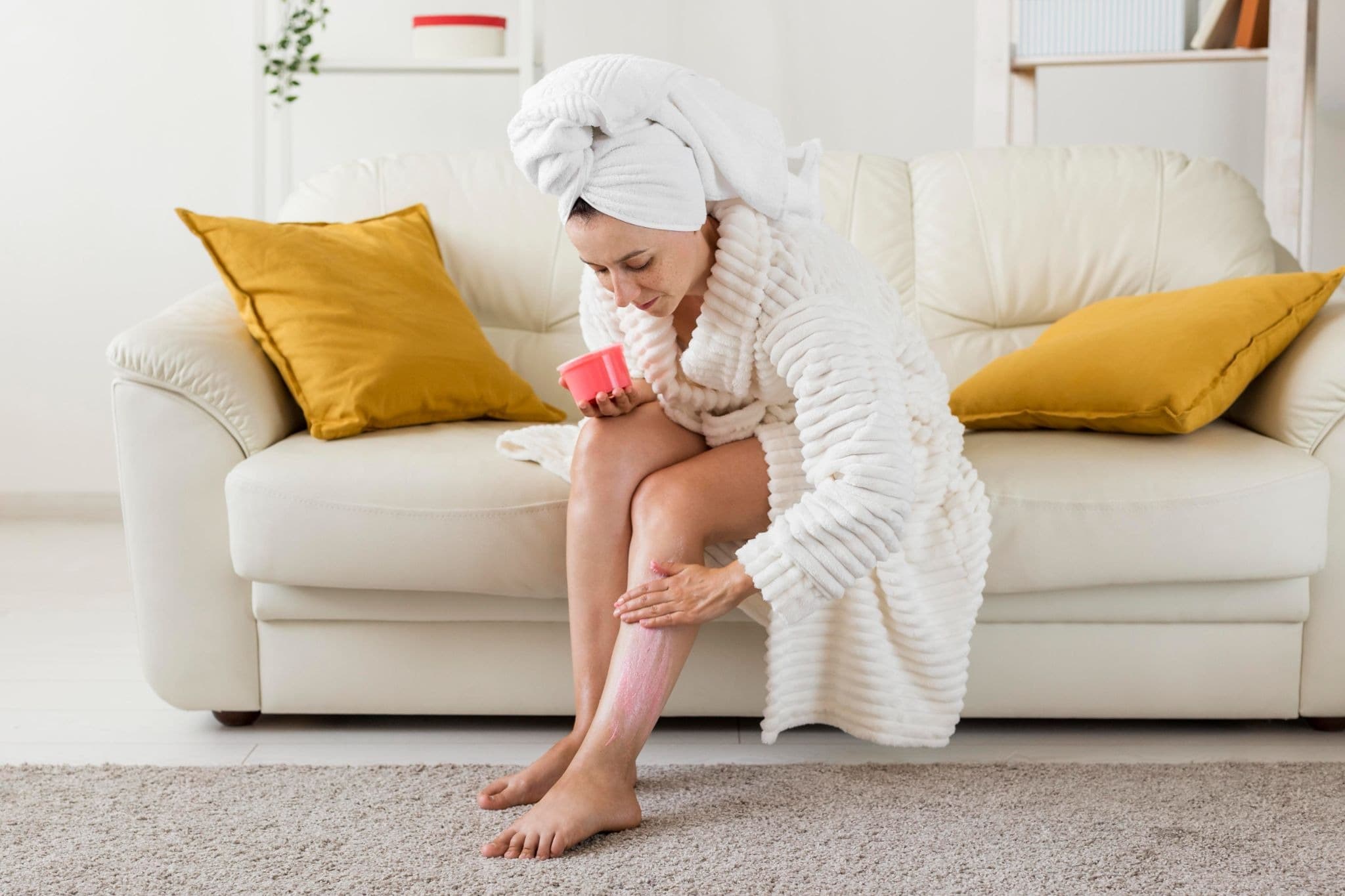 A woman in a bathrobe applying a soothing cream to her leg after hair removal